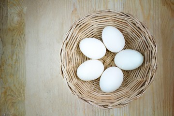 5 eggs in rattan basket on wooden background, lighten center