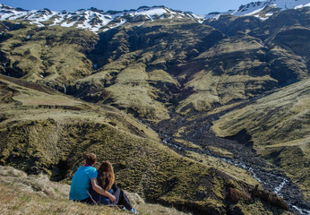 Fototapeta na wymiar Love in the nature. A couple sitting in the mountains looking at beautiful surrounding. A guy is hugging a girl. A lonely couple in the nature with no people around. Iceland.