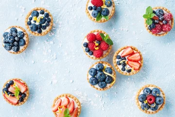 Foto op Canvas Delicious tartlets or cake with mixed berry on blue background from above. Summer pastry desserts. © juliasudnitskaya
