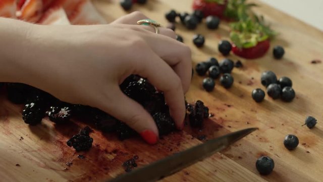 Close up over the shoulder of woman slicing berries on a wood cutting board