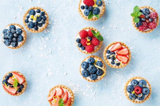 Delicious tartlets or cake with mixed berry on blue background from above. Summer pastry desserts.