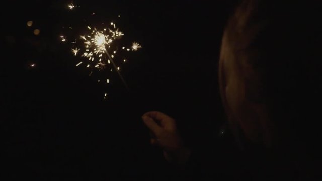Happy blonde girl smiling while holding a sparkler at night in reverse