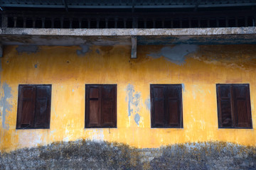 Wooden windows on old yellow wall cracked from the wall, retro and Thai traditional and classic style outside of house.
