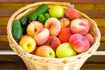 Woven from a vine basket stands on wooden boards filled with fruits from a fresh harvest. Peaches, apples, cucumbers.