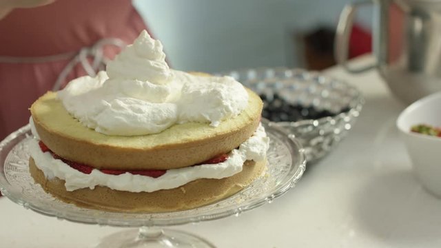 Woman spreads frosting all over a layer of cake