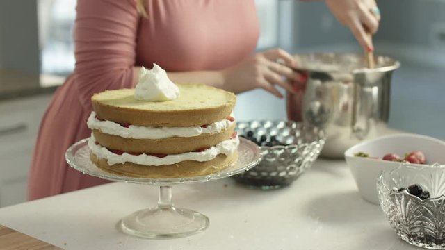 Woman spreads frosting on a cake in a bright sunny kitchen