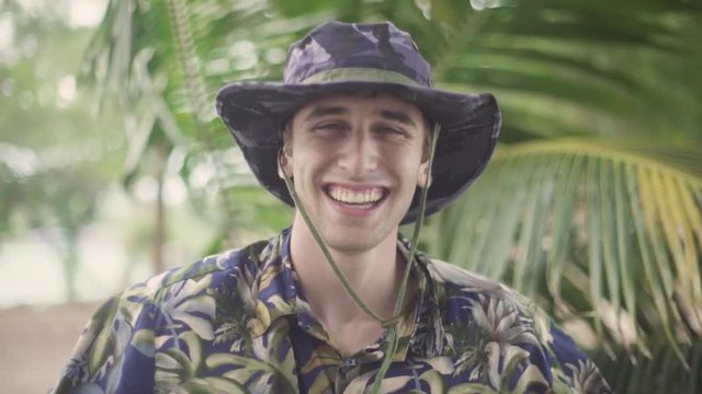 Happy young man in tropical explorer outfit smiling enthusiastically into the camera. Shot in tropical setting