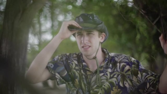 Safari explorer in tropical jungle puts on his hat as he explores environment