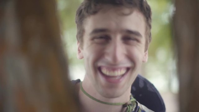 Happy Playful Man plays Peek-a-boo with camera through Trees in tropical Forest