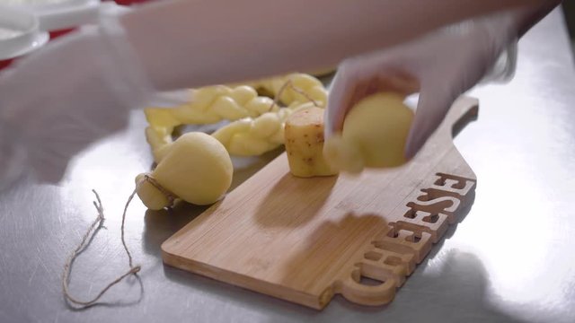 cheese maker is cutting final cheese product on a wooden chopping board on a table, close-up of hands