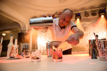 Barman adding cocktail ingredients on whiskey cocktails on bar counter