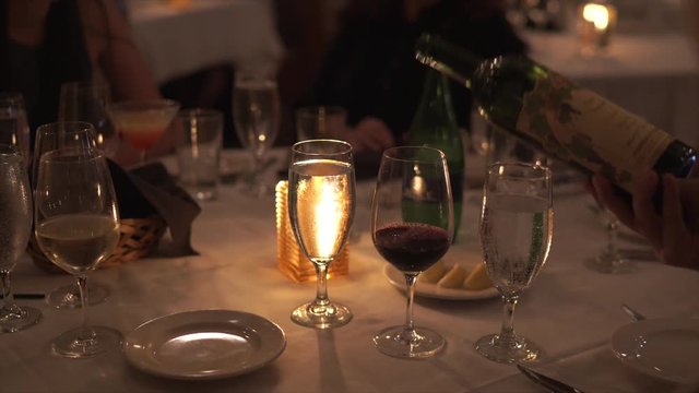Wine being poured at a large round, well decorated table in a fine dining restaurant. Woman then brings glass of wine to her mouth.