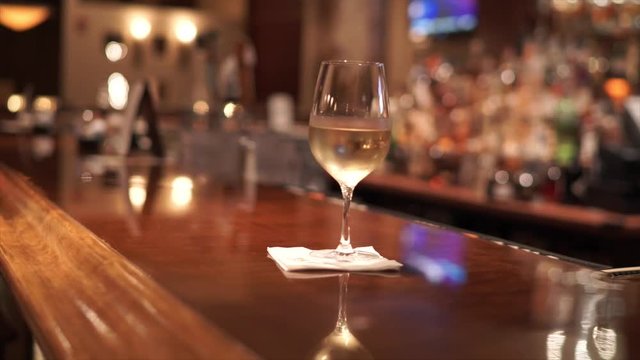 Male bartender delivers a glass of white wine to the bar in a fine restaurant.