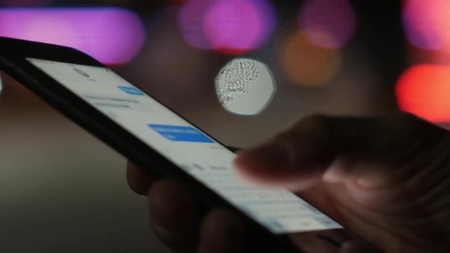 Typing and receiving chat messages on smartphone at night with bokeh color lights in background