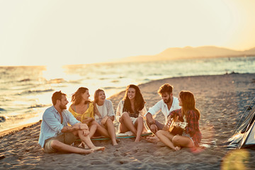 Young friends with guitar at beach. friends relaxing on sand at beach with guitar and singing together.
