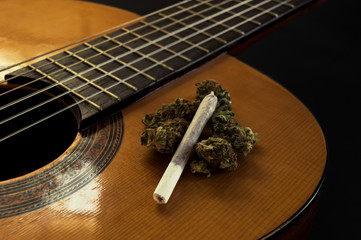 Fretboard and body of a classical or spanish guitar with marijuana buds and joint on it. Black background with blur effect. Close up view.