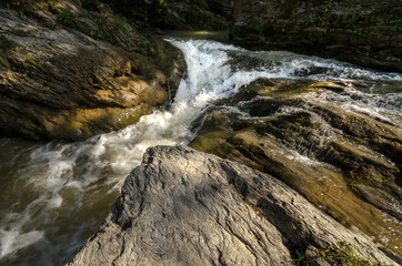 Wide angle shot of mountain river with a waterfall flowing between rocky coasts. Expressive foreground. Taken from low point of view at sunny spring day at Carpathian mountains. Natural background. 