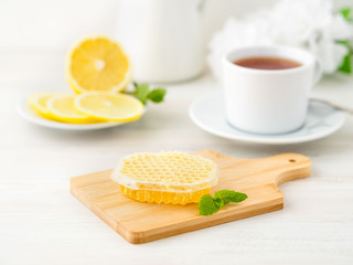 White Cup of tea, honey, honeycomb, lemon on white background. Folk method of treating colds. Side view, selective focus