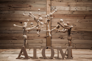wooden puppets with atom word and atom construction on wood table in wood .scene