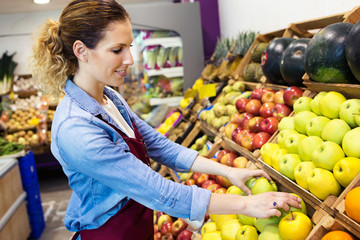 Saleswoman selecting fresh fruit and preparing for working day in health grocery shop.