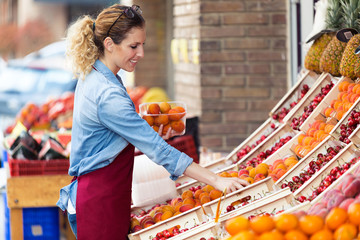 Saleswoman selecting fresh fruit and preparing for working day in health grocery shop.
