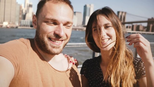 Smiling happy Caucasian young couple stand at epic New York skyline view of Manhattan, kiss and make a selfie photo.