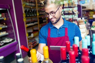 Handsome young salesman selecting a wine bottle in health grocery shop.