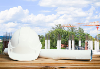 white safety hat and paper plan blueprint on wood table in working construction site housing building with copy space add text