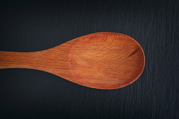 Empty wooden spoon on black slate background