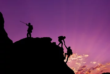 Schilderijen op glas Hikers climbing on rock, mountain at sunset, one of them giving hand and helping to climb.Teamwork , Helps ,Success, winner and Leadership concept . © osmanpek