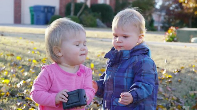 A toddler boy and girl fight over a camera during a wintry afternoon