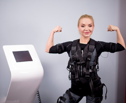 stong positive blond fit girl wearing EMS costume is showing her muscles during workout in the modern gym. sport and hobby concept