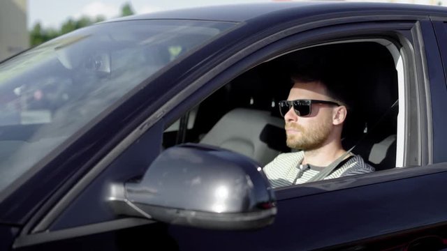 Stylish successful man driving a black luxury car in summer.