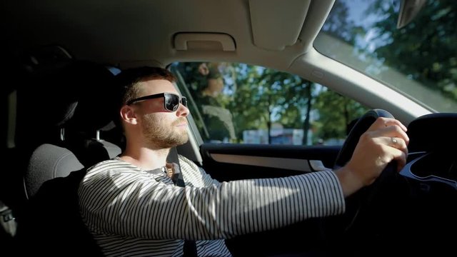Side view shot of a stylish man driving a car in city in summer.