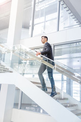 Young smiling businesss man walking up  the stairs  of a public building  and using a smartphone. Business, technology and communication concept