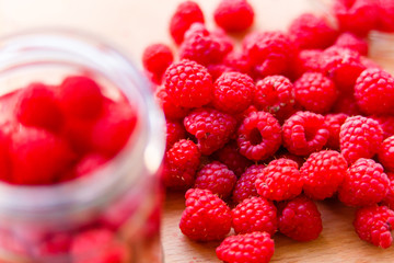 Ripe red raspberries lying on wooden board near jar