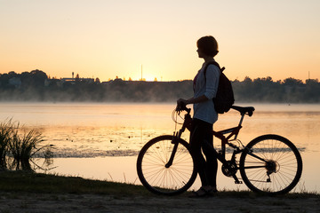 Obraz premium A girl with a bike near the lake in the summer morning