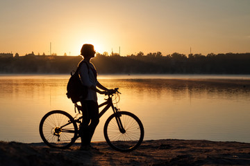 A girl with a bike near the lake in the summer morning