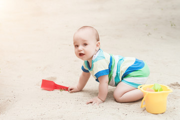 A little boy playing on a white sand. Child with toys for the sandbox. Baby crawling on a sandy beach