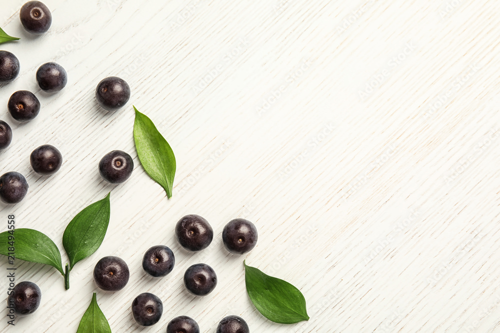 Wall mural Flat lay composition with fresh acai berries and leaves on wooden background