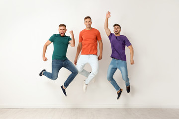 Fototapeta na wymiar Group of young men in jeans and colorful t-shirts jumping near light wall