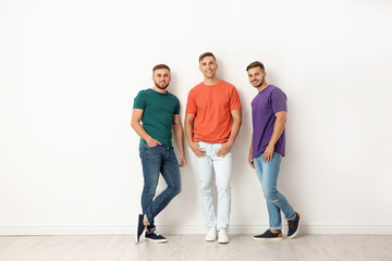 Group of young men in jeans and colorful t-shirts near light wall