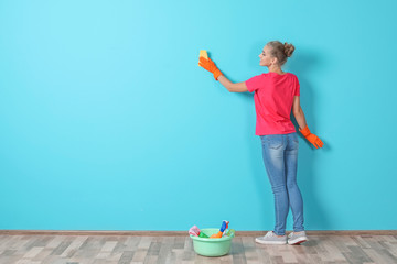 Woman in gloves cleaning color wall with rag