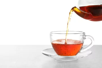 Poster Pouring hot tea into glass cup on white background © New Africa