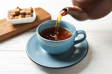 Pouring black tea into ceramic cup on wooden table