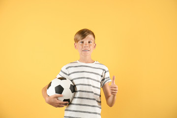 Portrait of young boy holding soccer ball on color background