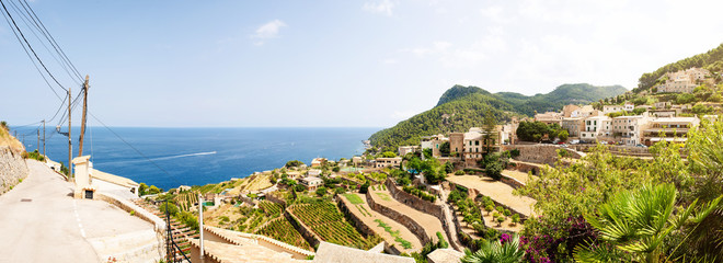 panoramic shot of typical village and landscape against blue sea and sky on island of Mallorca,...