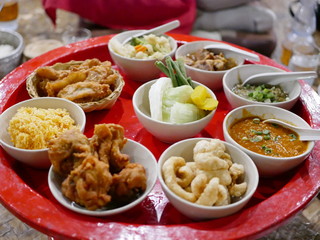 Northern Thai customary style dinner (khantoke) with variety of local menus being served family-style on large platters at low tables while guests relax on floor mats
