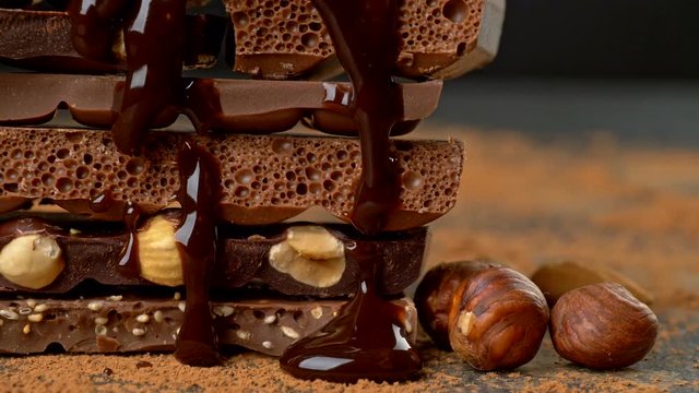 Melted chocolate pouring over heap of broken pieces chocolate and nuts. Slider shot. UHD, 4K