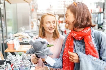 Young pretty hipster girls friends having fun outdoor on the street. Shopping together for cute souvenirs and toys